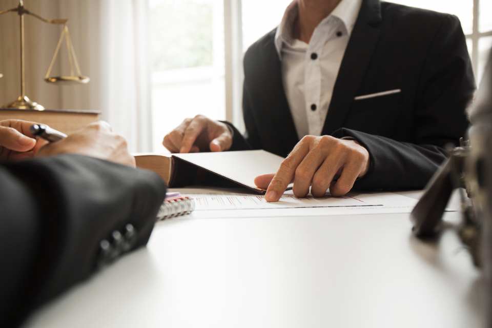 Hombre de traje señala algo en un documento mientras lo compara con algo en un libro de derecho